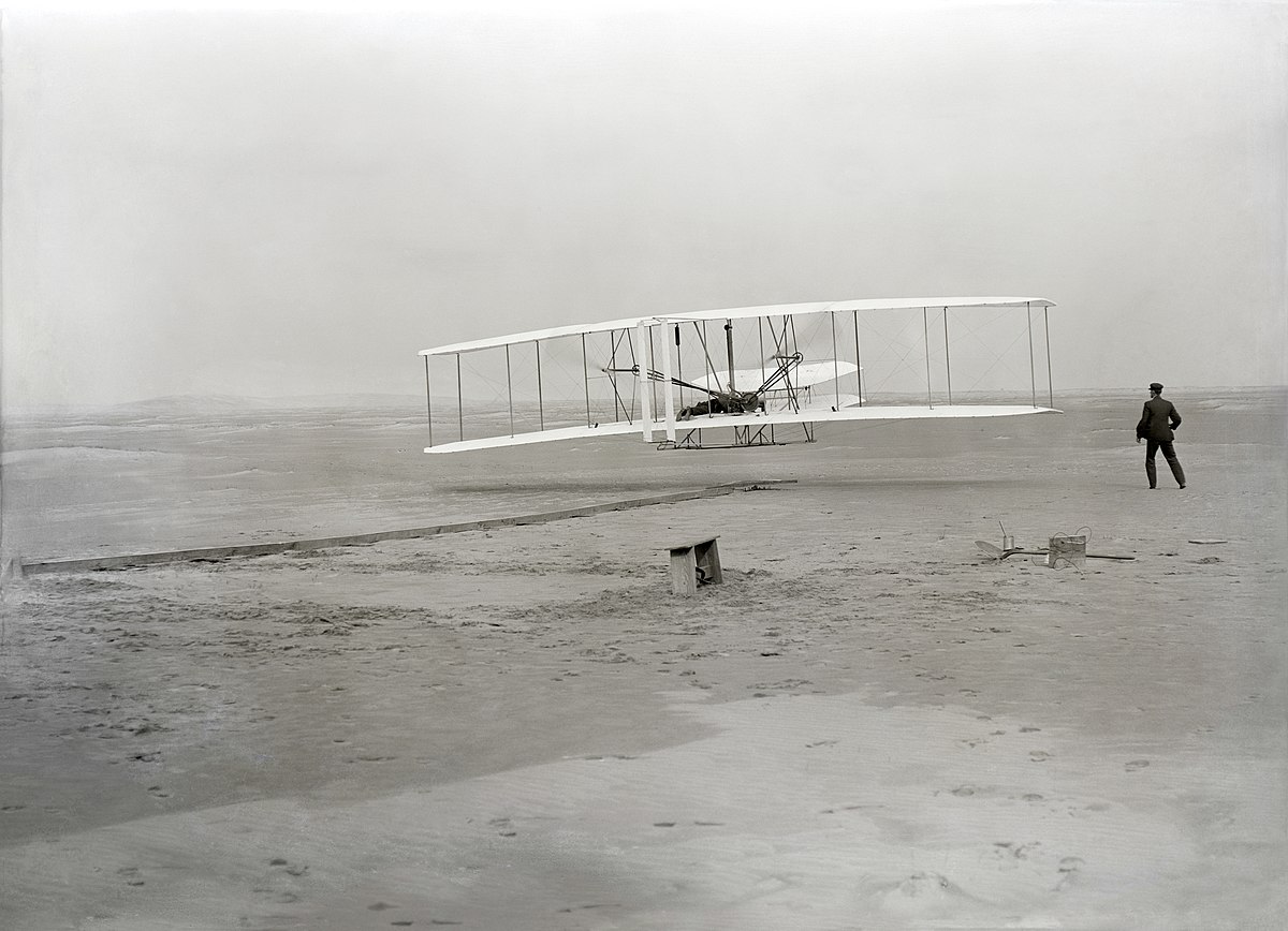 The Wright Brothers’ first powered flight, December 17, 1903, at Kitty Hawk, North Carolina. Photo by John T. Daniels. Public domain, via Wikimedia Commons.